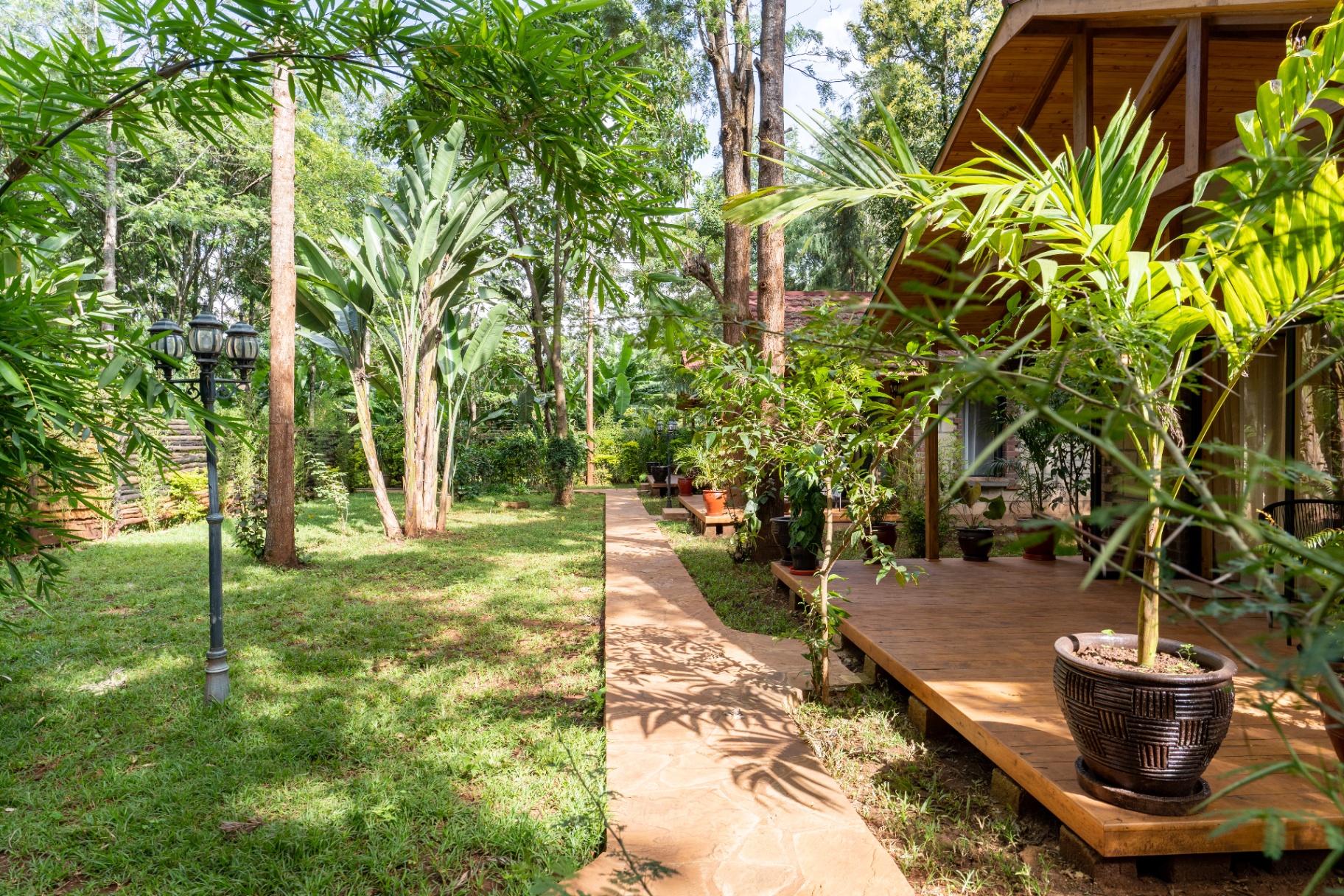 Garden path view past bamboo and tropical trees toward the Cottage 1 deck and veranda, with lawn, lamp post and layered greenery framing the facade