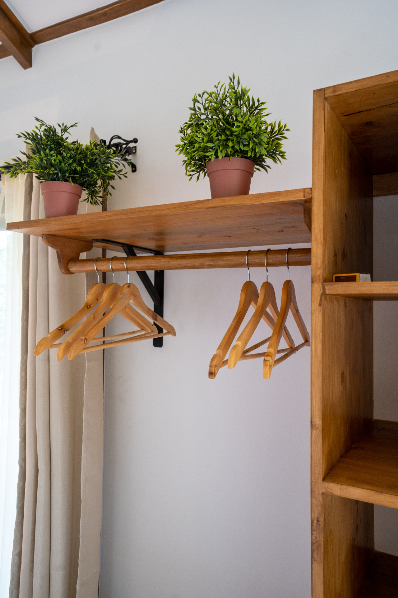 Detail of the open timber wardrobe in Cottage 2 with wooden hangers, built-in shelving and small potted plants above the rail