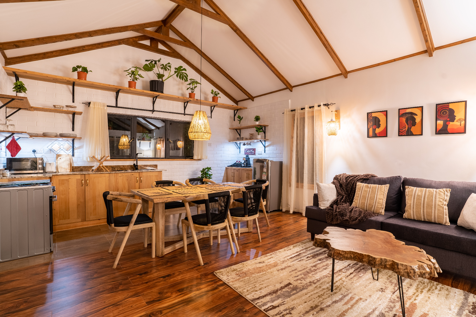 Sweeping view of Cottage 1's open-plan interior with kitchen, dining table for six and lounge under a soaring beamed ceiling lined with potted plants