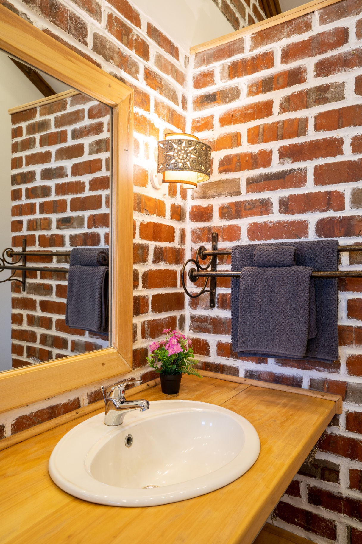 Vanity corner with folded slate-blue towels on a wrought-iron rail beside the mirror and brick wall