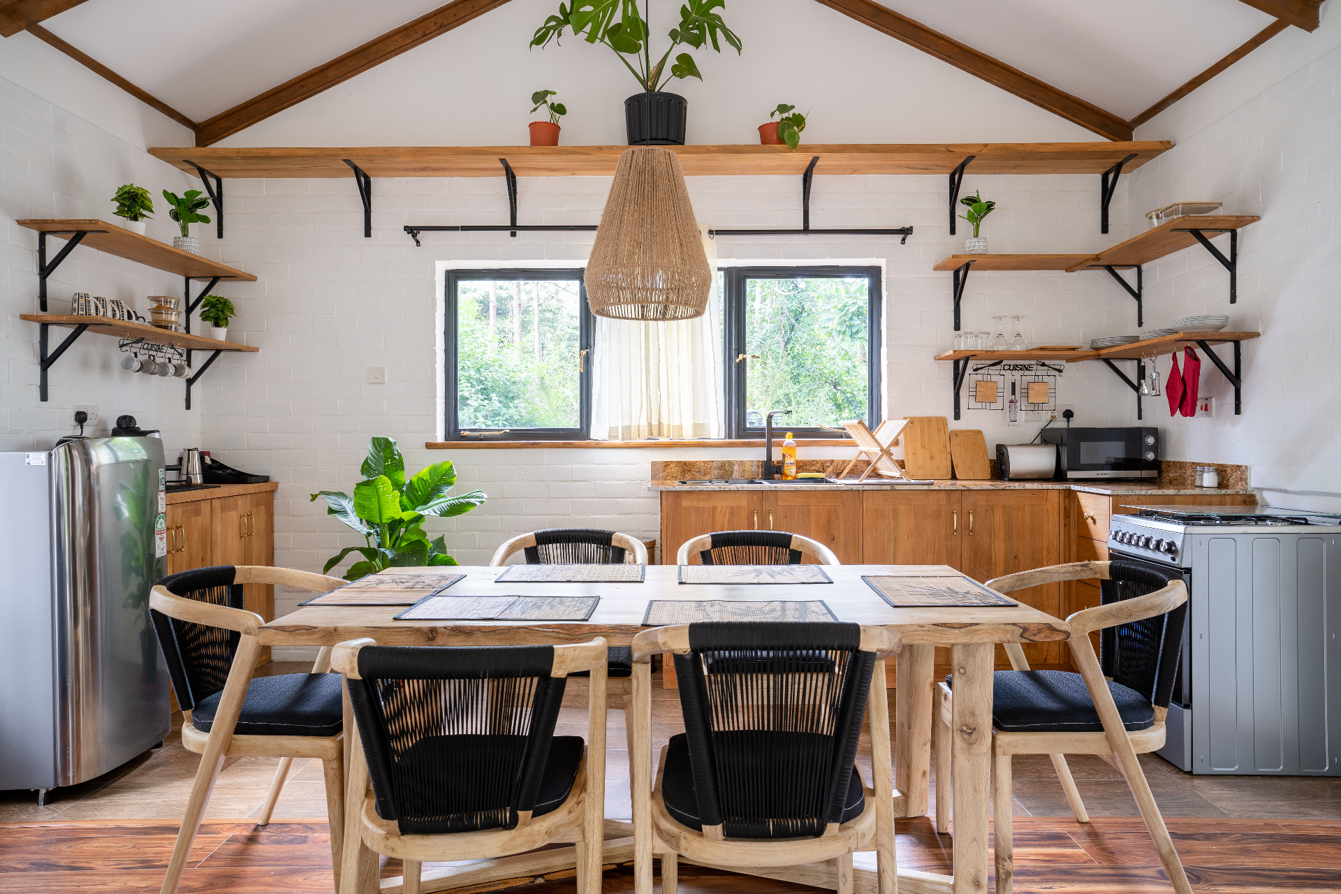 Head-on view of Cottage 2 kitchen with timber cabinets, granite counters, open shelves of glassware and dishes, gas range, and a six-seater dining table in the foreground