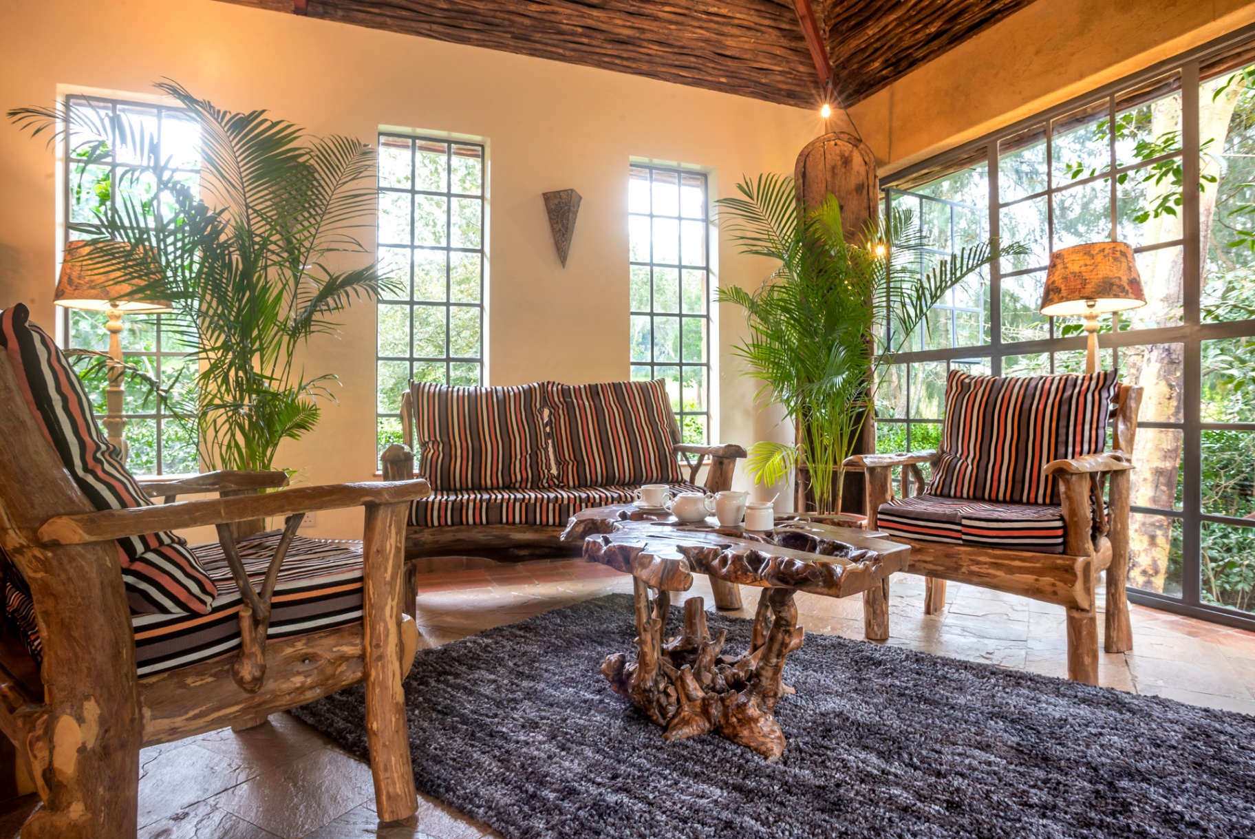 Sunlit sitting corner with striped-cushion armchairs, palms and tall garden-facing windows