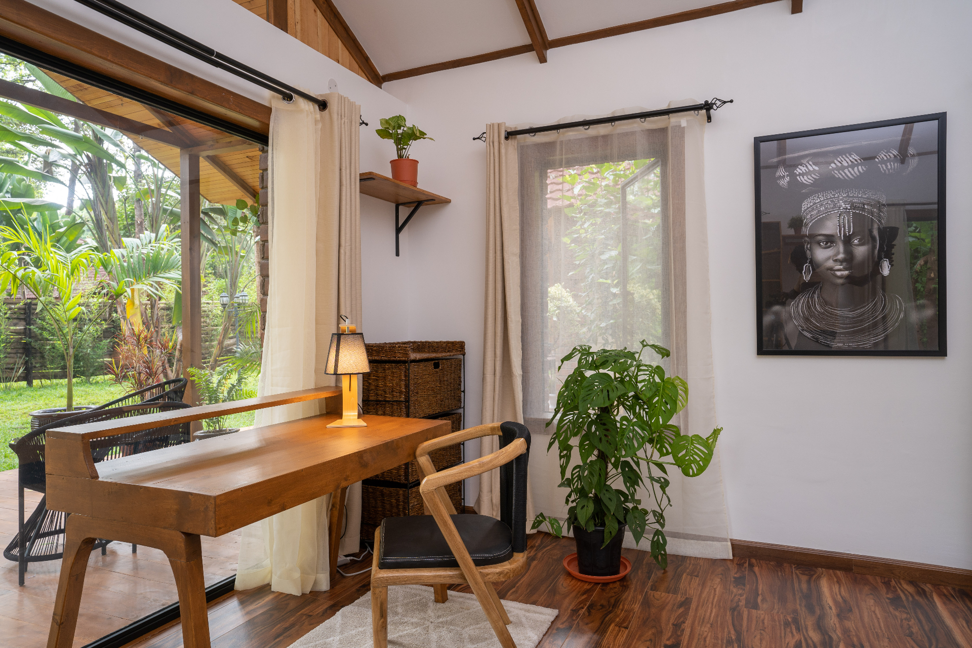 Cottage 2 bedroom study nook with timber desk, wicker storage, framed portrait artwork, monstera plant and sliding doors opening to the tropical garden