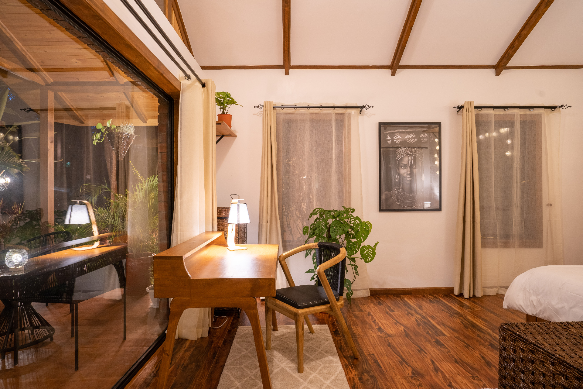 Nighttime desk corner in Cottage 2 with a timber writing desk, chair, warm table lamp, framed portrait and reflections in the large glass doors