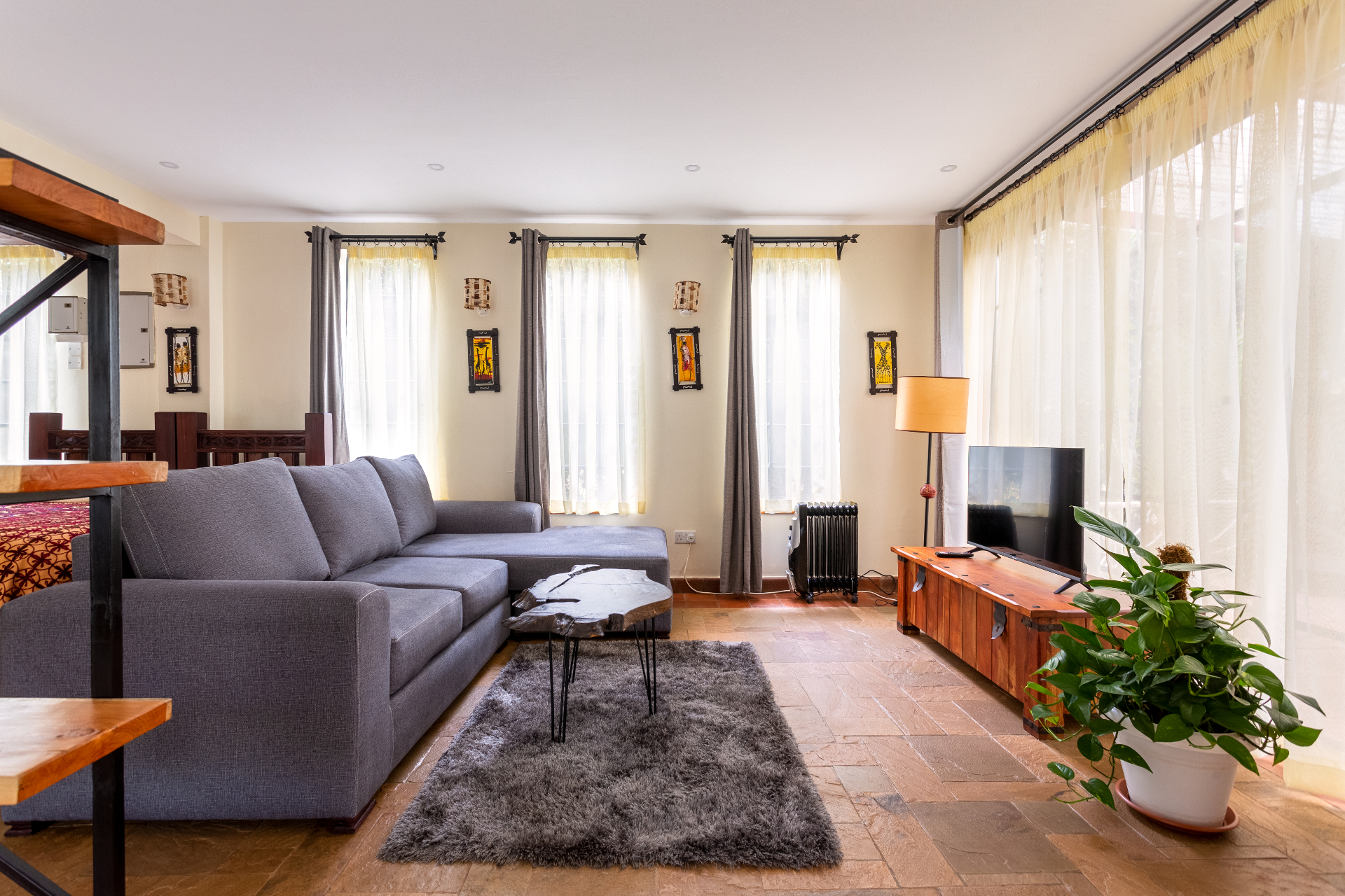 Living area with grey sectional sofa, live-edge coffee table, television console and full-height corner windows