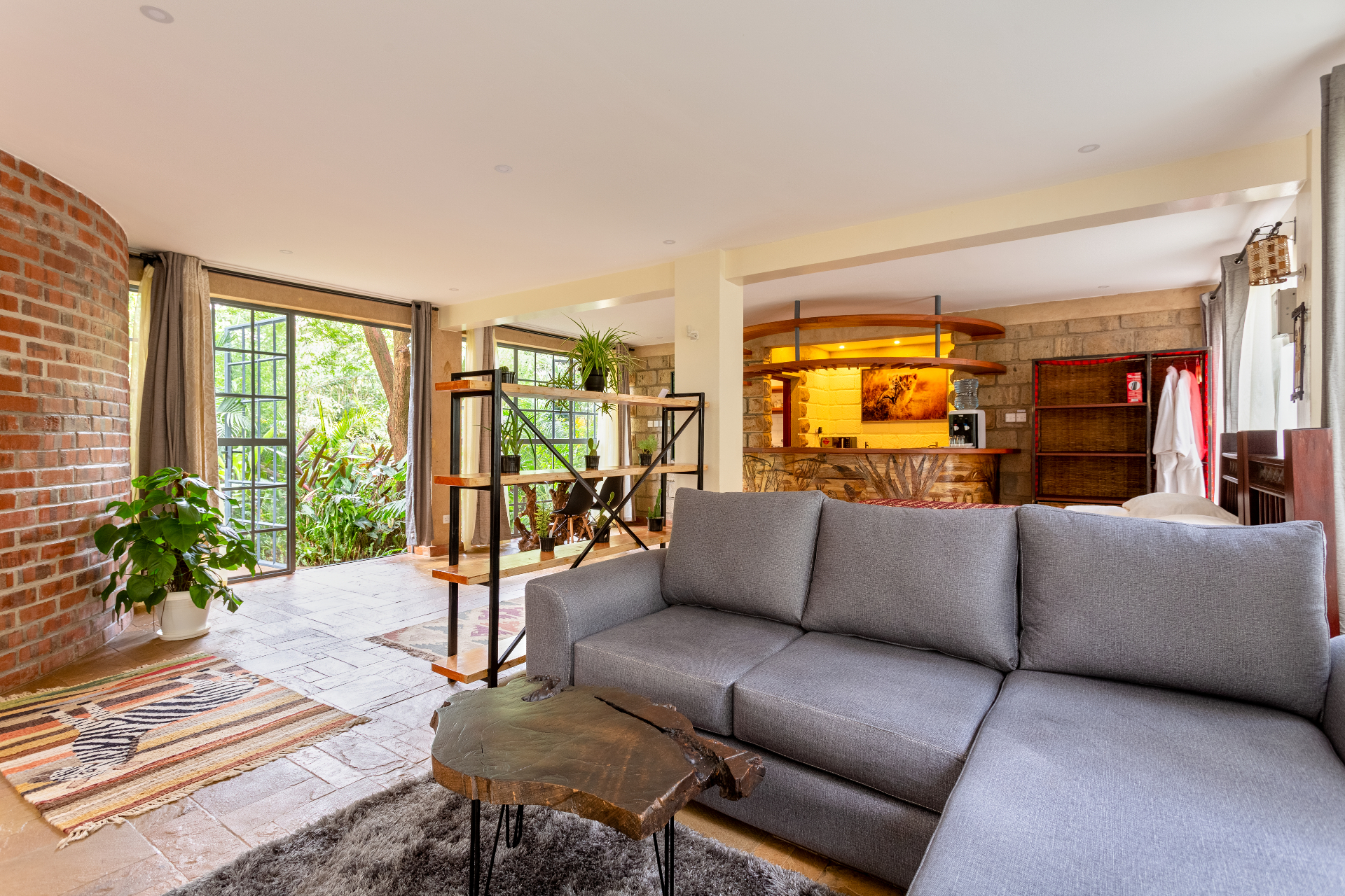 Lounge view toward the garden-facing windows and open-plan studio with sofa, divider shelving and kitchenette beyond