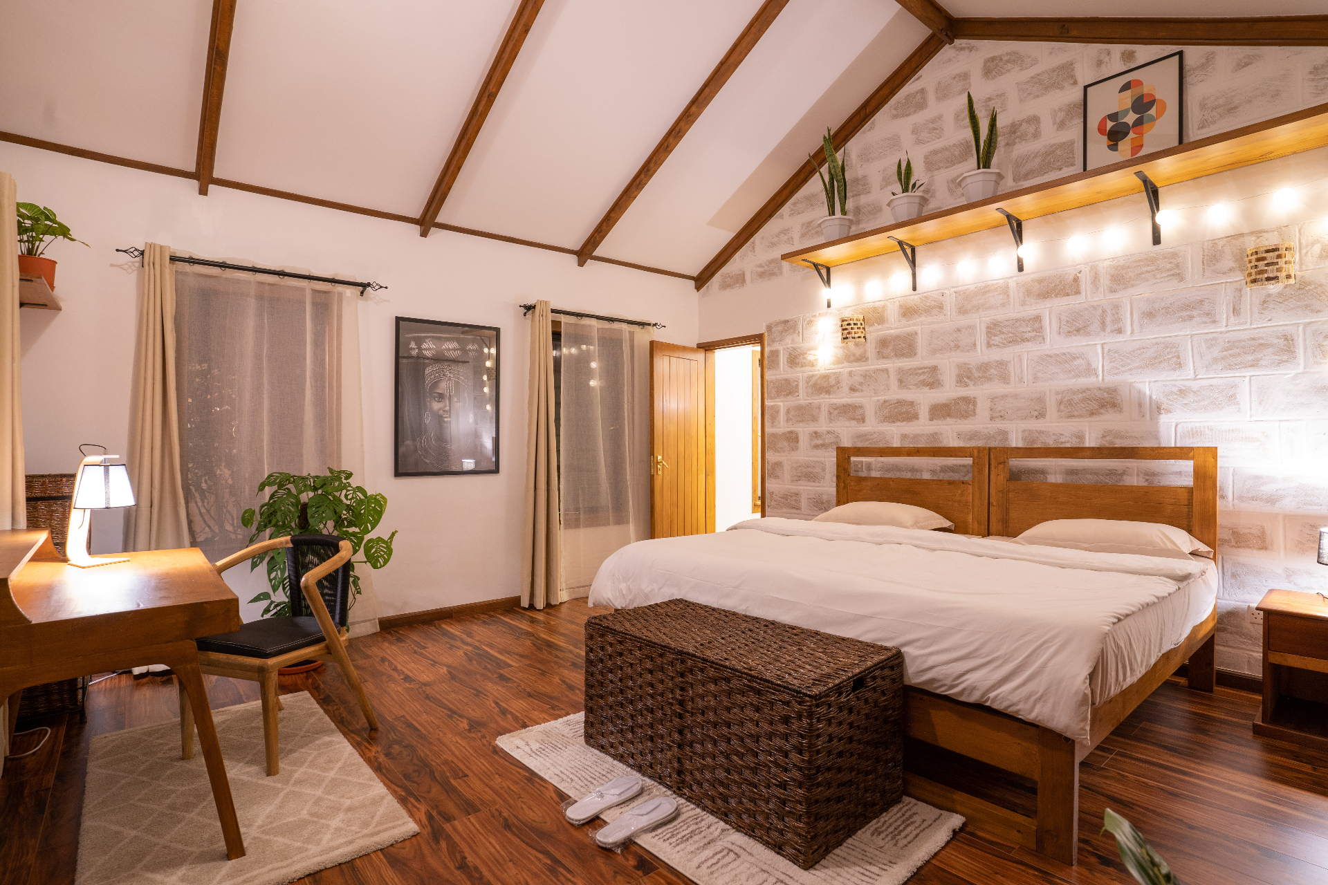 Wide evening view across Cottage 2 showing the bed, timber floor, desk corner, wicker bench and warm accent lighting under the vaulted ceiling