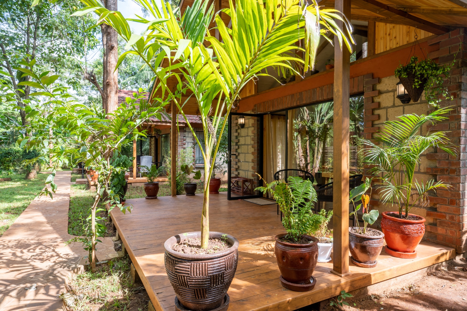 Angled exterior view of Cottage 1 showing the timber deck, sliding glass doors, potted palms and layered tropical planting around the veranda