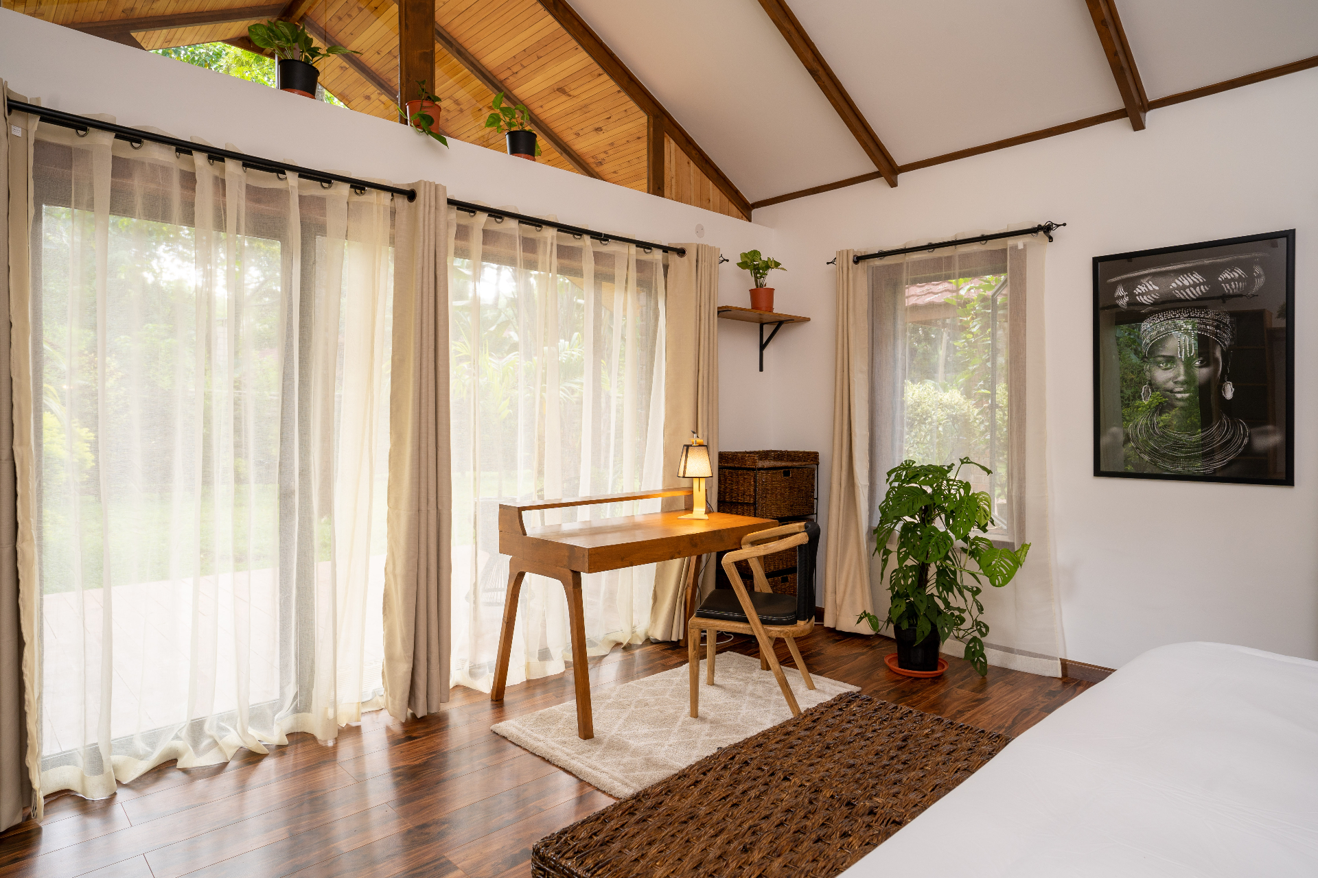 Cottage 2 bedroom corner with a timber writing desk, sheer curtains, potted monstera, framed portrait and high timber-lined ceiling lit by garden daylight