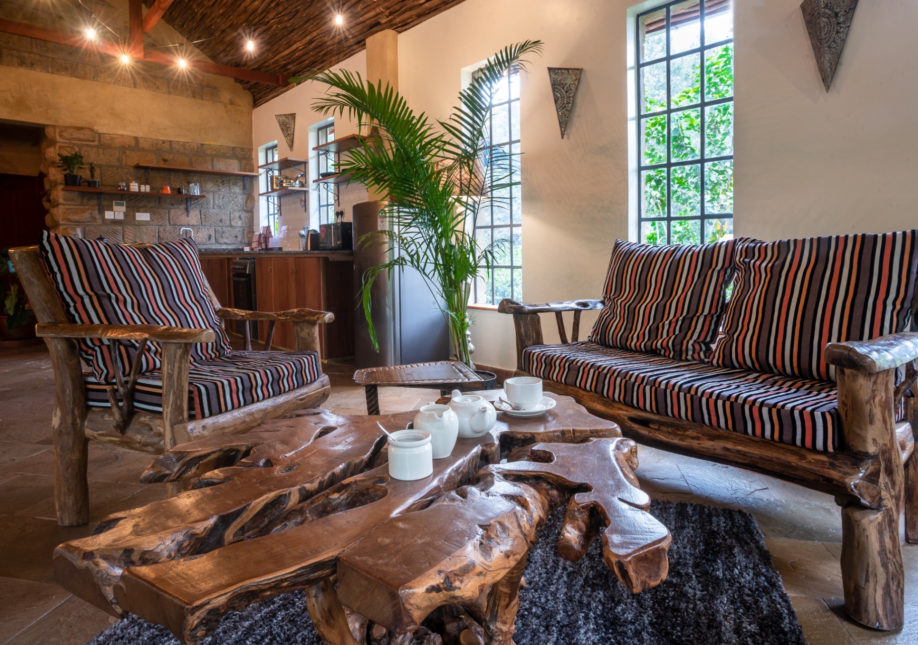 Rustic timber sofas with striped cushions around a live-edge coffee table, with a small kitchen bar behind