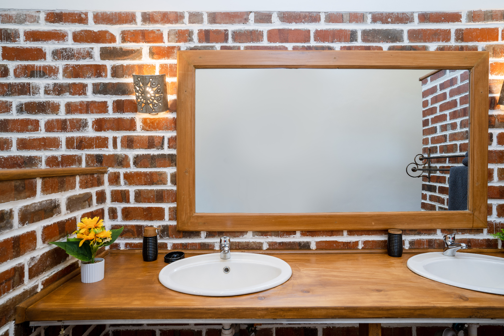 Close view of Cottage 2 double sink vanity with timber counter, twin white basins, large framed mirror and sunflowers against a whitewashed brick wall