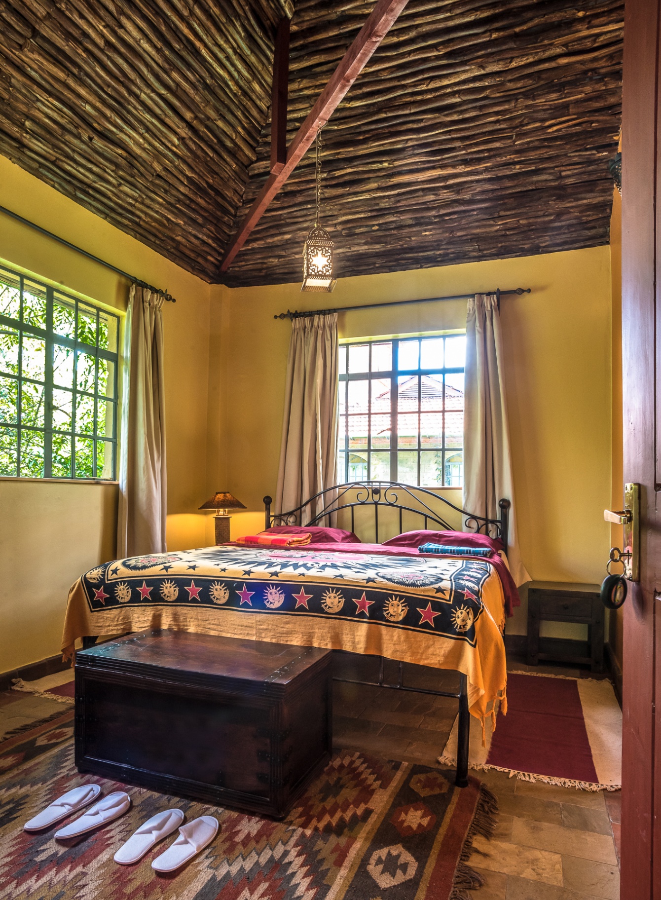 Bedroom with iron bedframe, cream curtains and a high dark timber ceiling