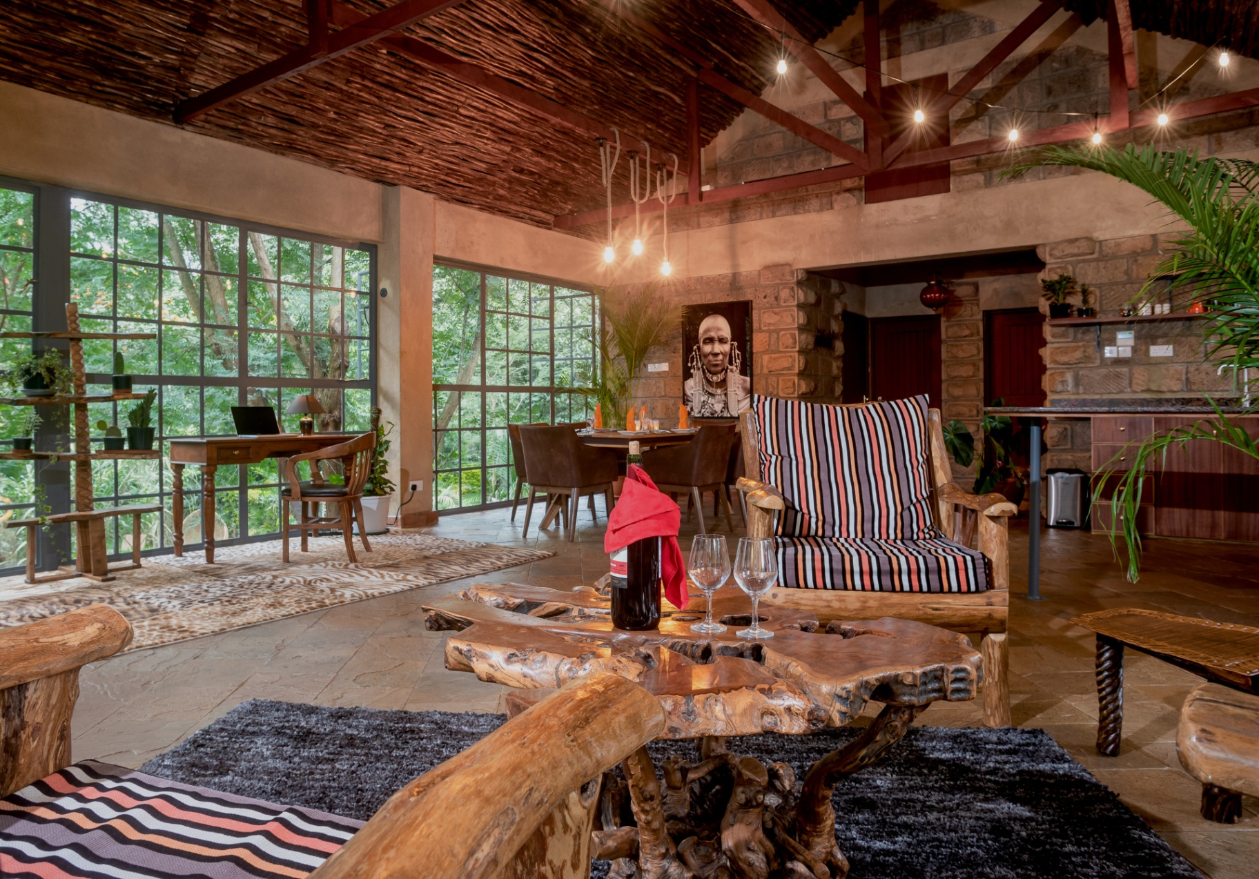 Open-plan lounge, dining and workspace under a vaulted thatched ceiling with jungle views through steel-framed windows