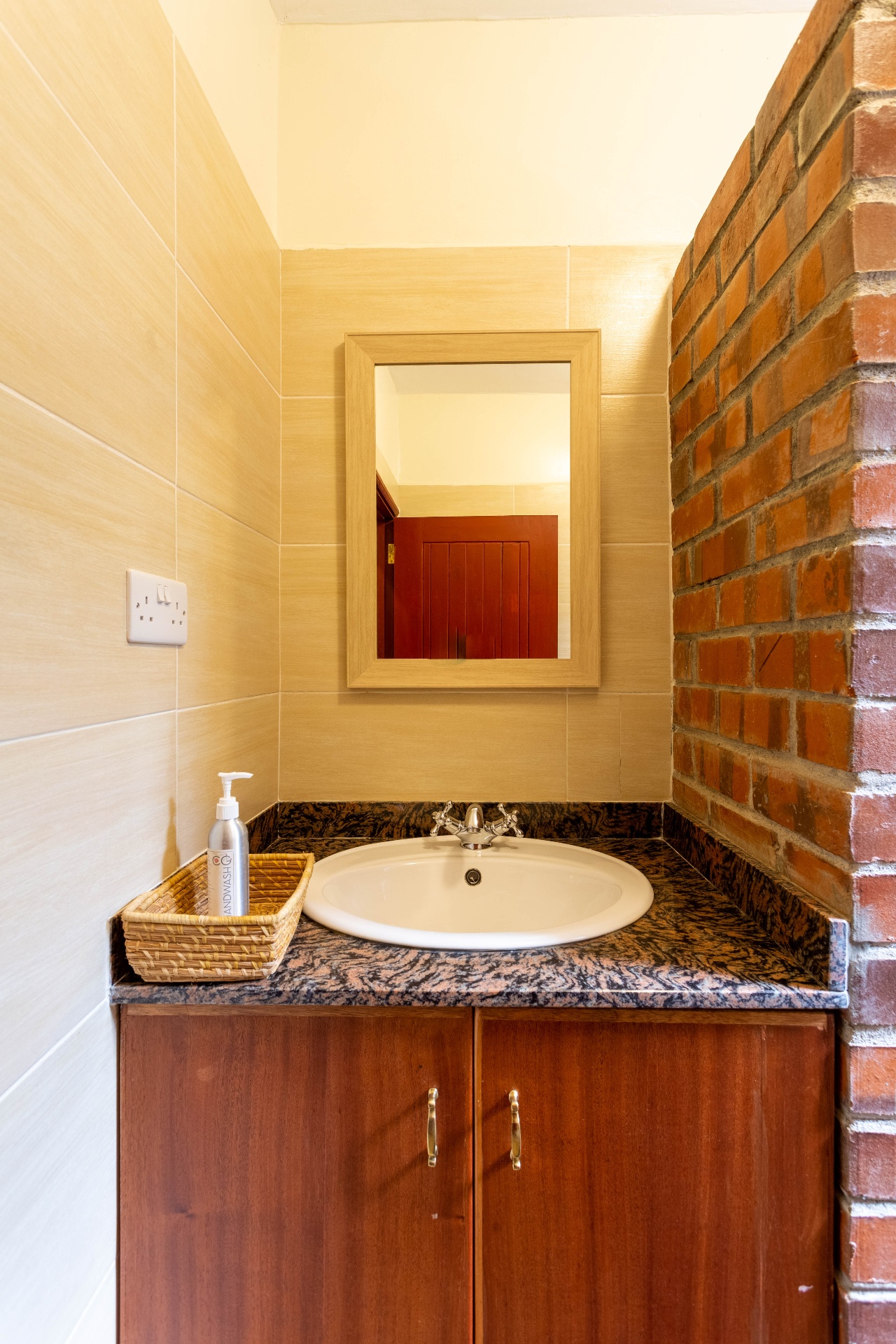 Bathroom vanity with granite top, framed mirror, hand-wash pump and exposed red-brick corner wall