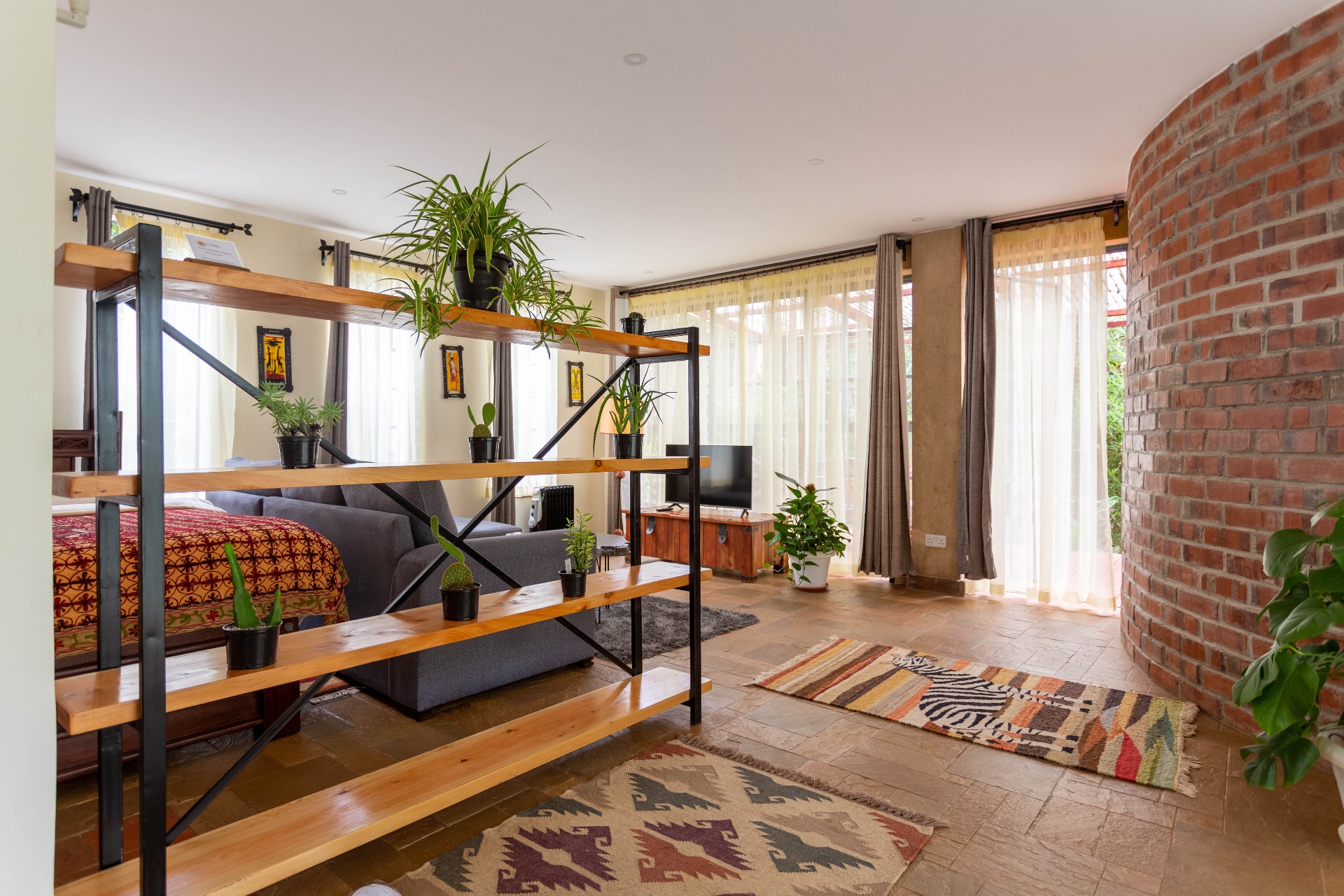 Lounge area with sheer curtains along floor-to-ceiling terrace doors and a curved exposed-brick feature wall