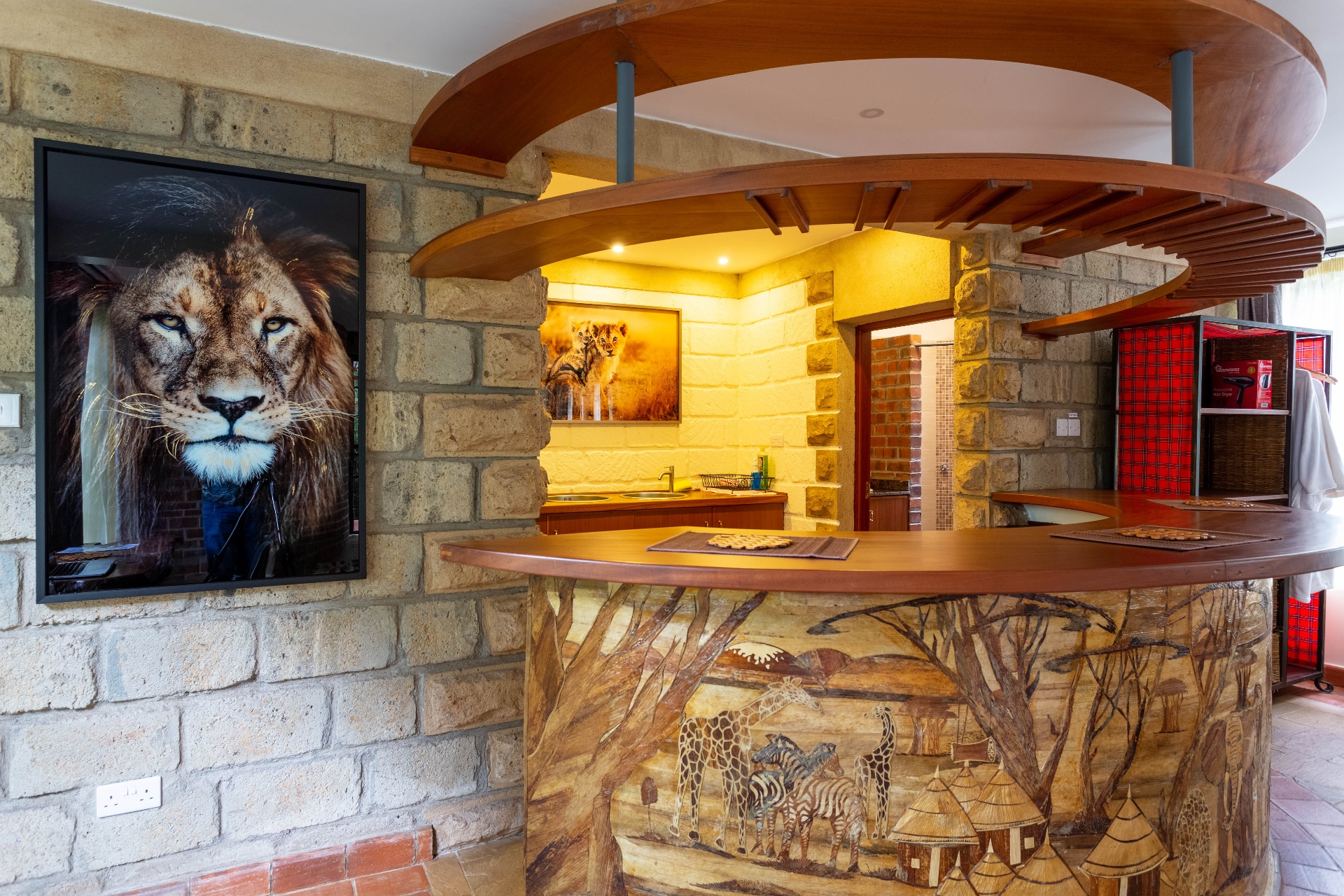 Curved timber bar with hand-painted safari mural base, next to a large framed lion portrait on the exposed-stone wall