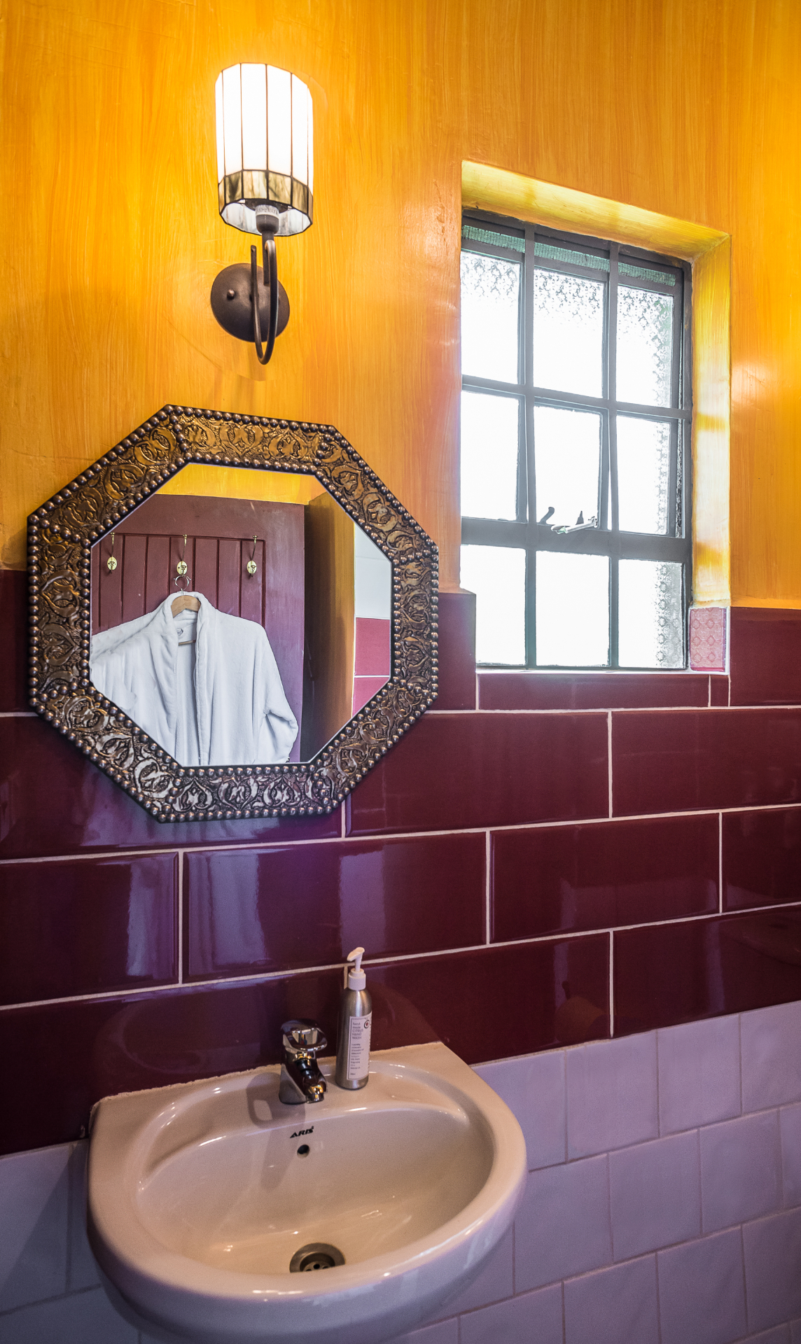 Bathroom vanity with an octagonal patterned mirror, ochre walls and glossy plum subway tiles