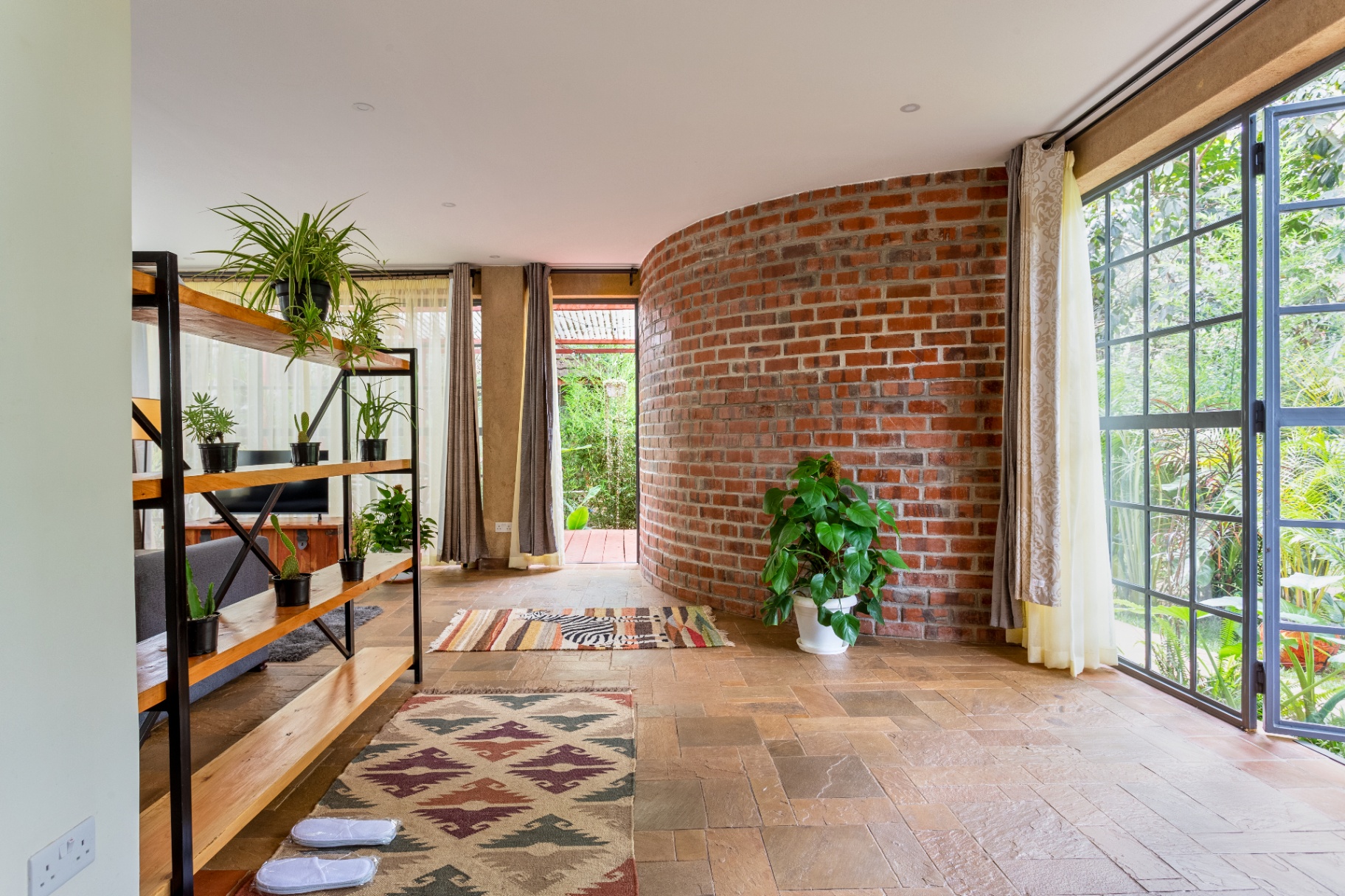 Open studio floor area with curved exposed-brick wall, garden-facing windows and terrace access beyond the divider shelves