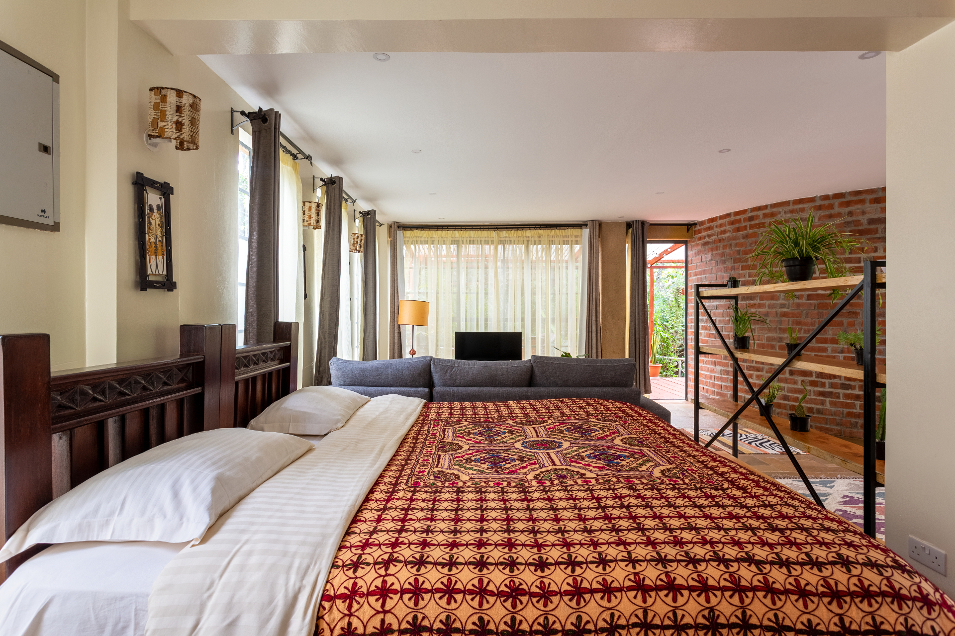 Carved dark-timber bed with patterned throw looking across the lounge toward the terrace doors and curved brick wall